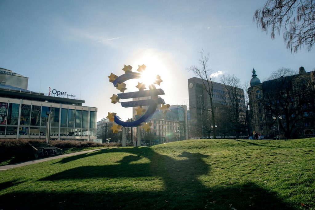 Euro sculpture in Frankfurt, Germany with cityscape buildings and sunlight.