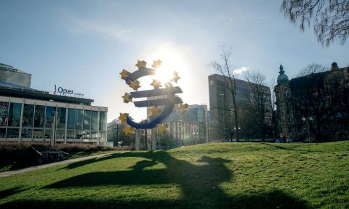 Euro sculpture in Frankfurt, Germany with cityscape buildings and sunlight.