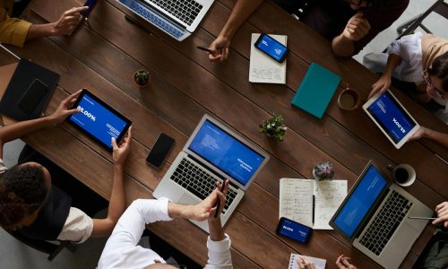 Overhead view of a diverse team discussing around a wooden table, using technology.