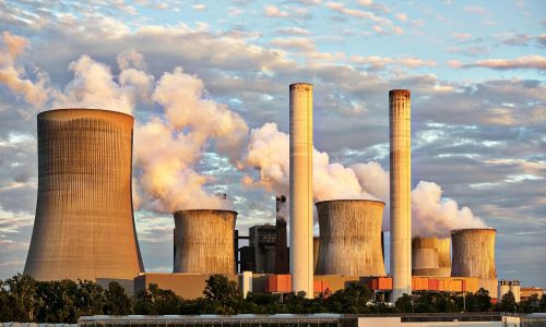 View of a power plant with smoke emissions under a cloudy sky, depicting industrial energy production.