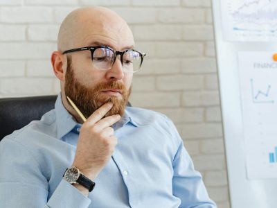 Bearded man in blue shirt contemplating financial data on whiteboard indoors.
