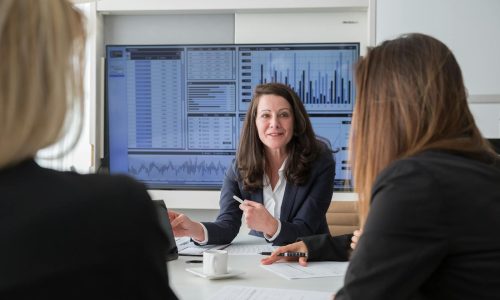 Professional businesswomen engaged in a meeting discussing data on a screen.